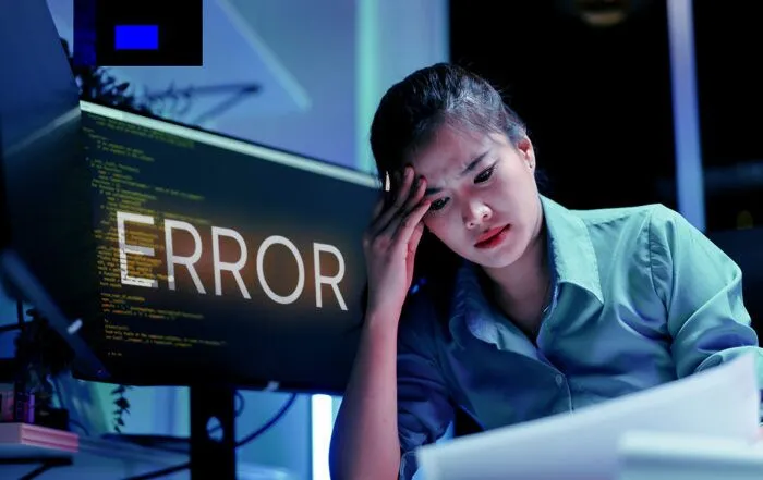Frustrated and stressed business woman sifts through code with error sign on her computer
